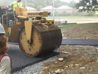 A crew member rolls out recently poured pavement to make the surface smooth.