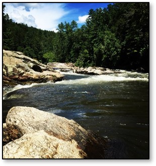 A river with flowing water, rocks, trees, blue sky and clouds