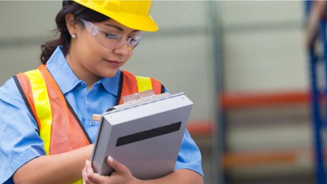 Inspector maintaining record on clipboard in factory