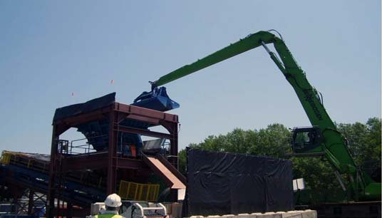 Workers at the processing facility use excavators with environmental clamshell buckets to load the contaminated sediment and debris onto a trommel which begins the process of separating the material.