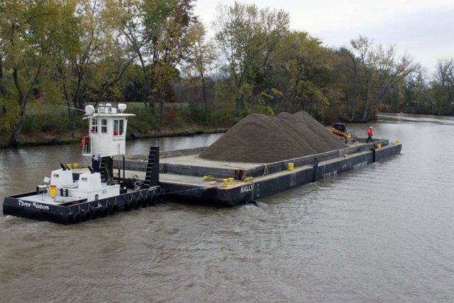 After an area has been dredged of contaminated sediment to the EPA's standards, clean backfill is transported on a barge by a tug boat. The backfill replaces dredged sediment and maintains the natural contours of the riverbed.
