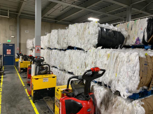 This photo shows what appears to be stacked rows of recyclable bundles. Unoperated fork lifts are on the ground next to the piles.