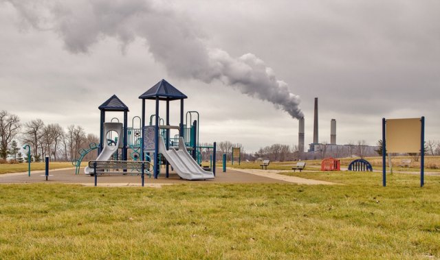 A plume of emissions rises from a factory smokestack near an empty playground