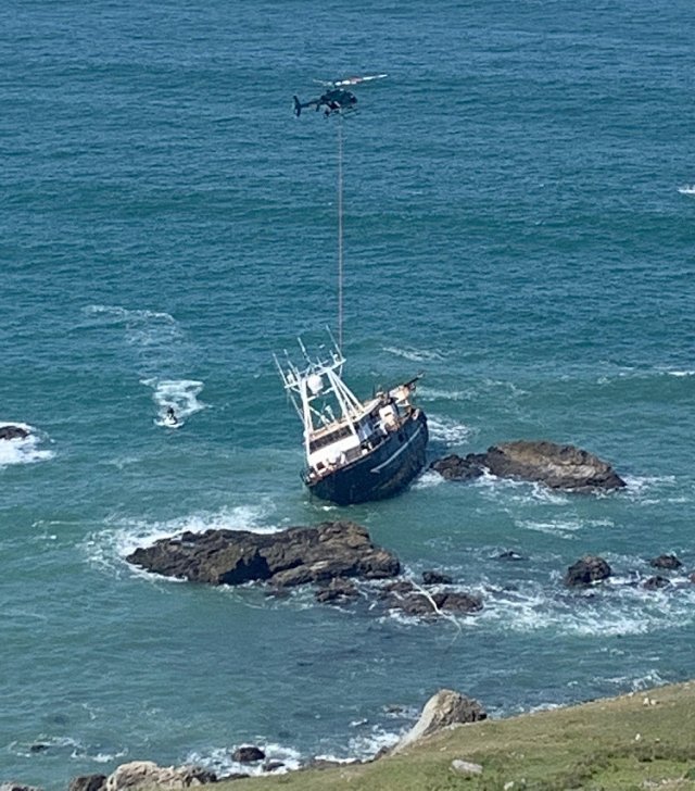 Helicopter with rope leading down to boat on rocky coastline