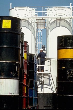 A man climbing a ladder between two large barrels of chemicals