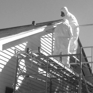 Picture of two people wearing protective coveralls standing on a scaffold on the outside of a house.