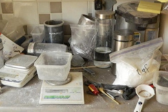 Various containers, cups, a plastic bag filled with white powder, and two digital scales sit on a countertop dusted with fentanyl residue