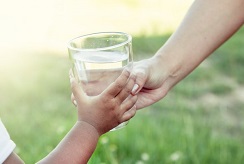 adult's and child's hand holding glass of water
