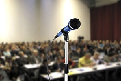 A microphone set up in front of a full audience at a public meeting
