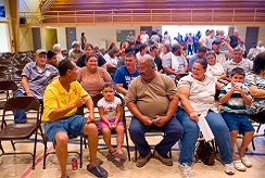 A crowd of people sit in folding chairs during a town hall meeting