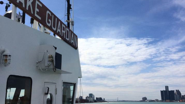 The Lake Guardian boat with The Ambassador Bridge in the background, ona partially cloudy day. The words Lake Guardian visible on the side of the boat.