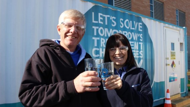 Two people smiling for the camera while holding glasses of clean water