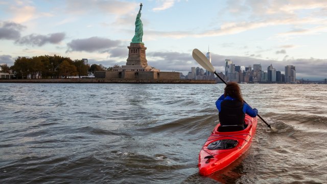 Person rowing a canoe with Statue of Liberty in the background