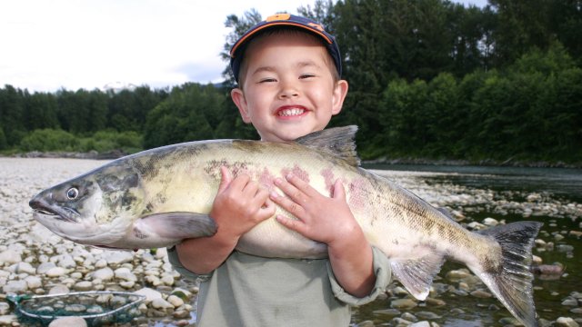 Young boy holding a large fish at a lake.