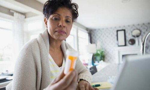 This is a picture of a woman looking at a bottle of medication 