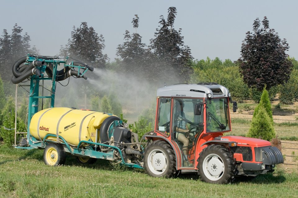 photograph of a tractor applying pesticides to an orchard