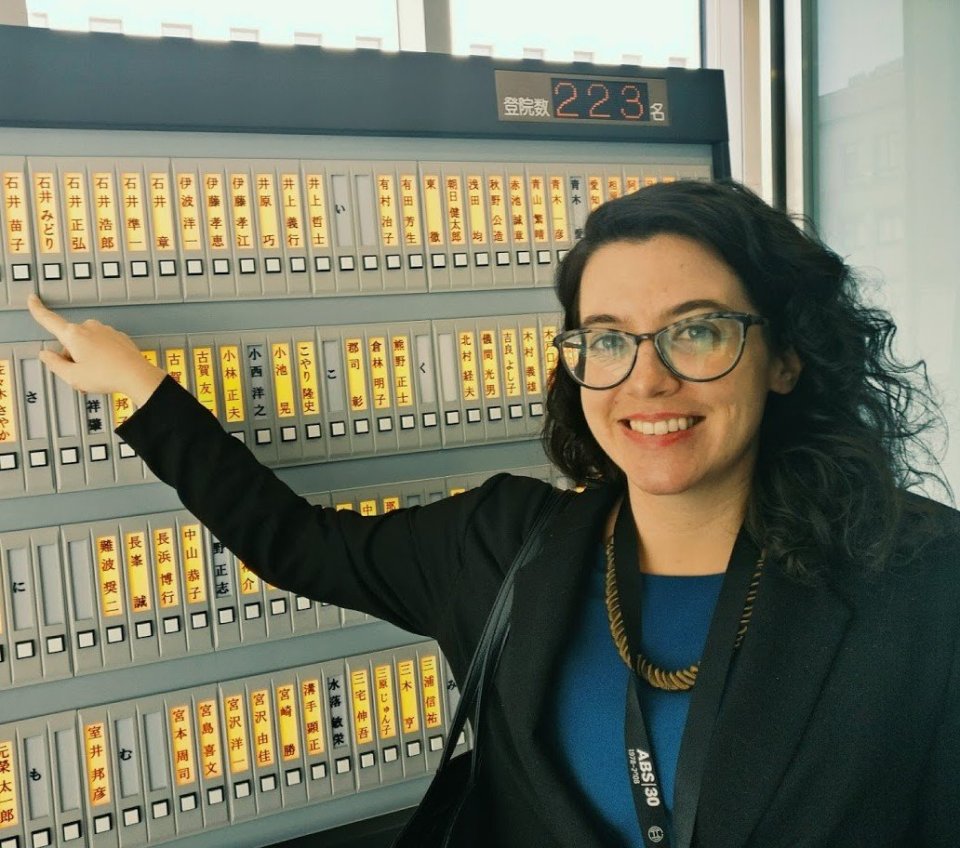 Researcher Sara Watson smiling at the camera and pointing at a machine.
