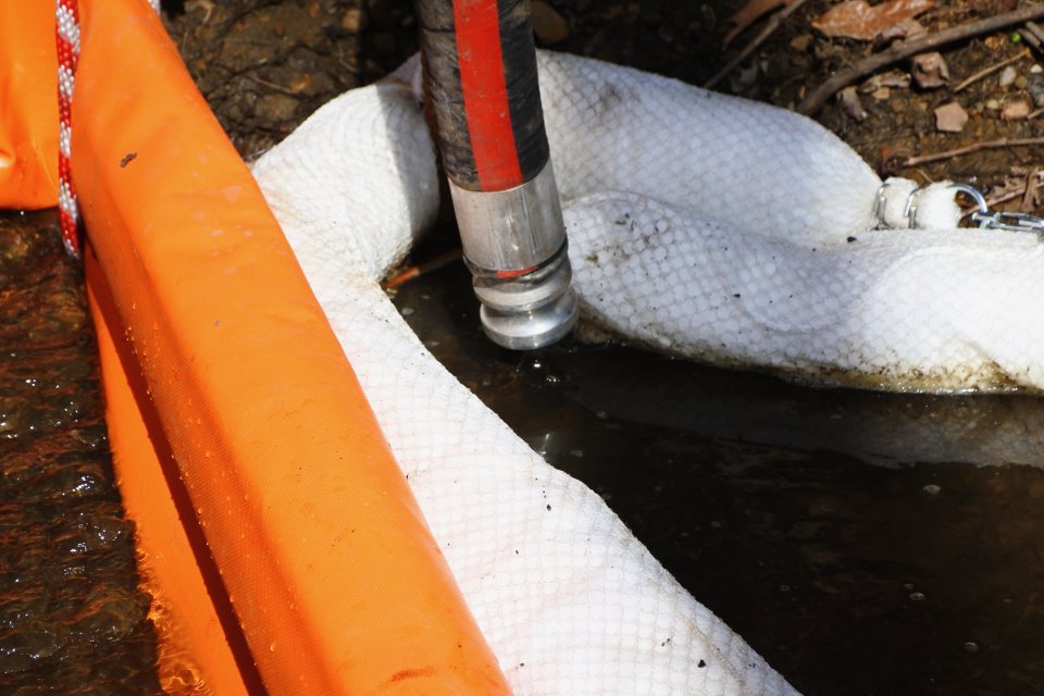 Vacuum trucks are placed near booms to collect oil sheen generated during stream and culvert cleanup