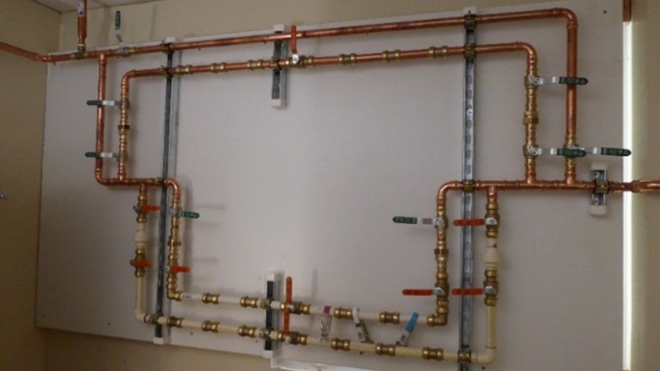 A plumbing system of copper, PVC, and PEX pipe on a wall.