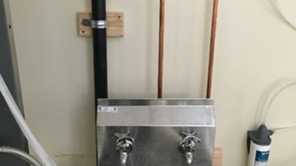 A metal utility sink hooked up to various plumbing components.