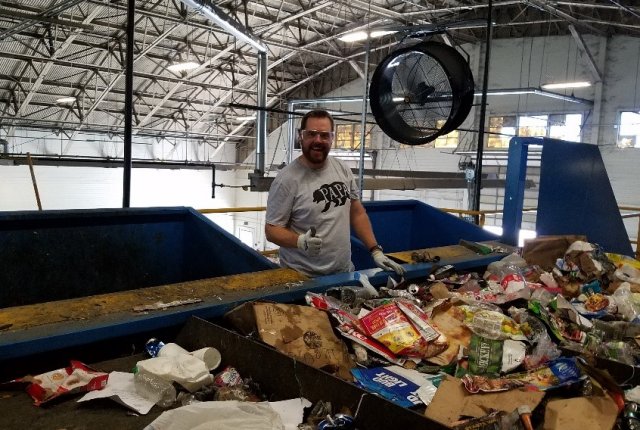 Photo of Mike Nye, Net Zero Program Manager, demonstrating how he would remove contaminants from recycling stream in a recycling facility.