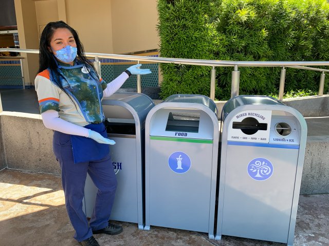 Image of a young woman showing off the food/compost bins at Disneyland. 