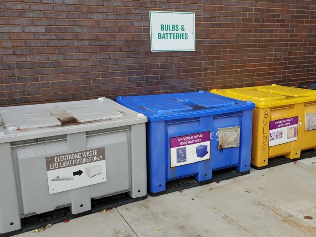 Several different colored recycling bins by a brick wall. 