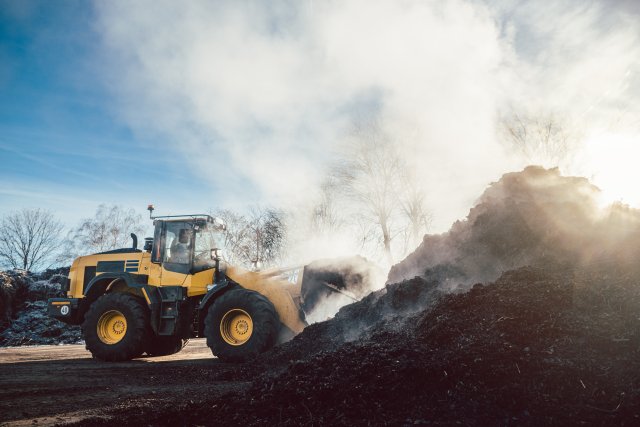 This is a photo of a yellow front loader pushing finished compost around a large compost yard