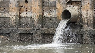 Stock photo of a storm water drain releasing water into a river or creek