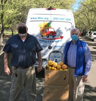 Two men standing in front of a truck with boxes of produce. 