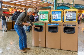 A man placing recyclables in an airport recycling receptacle. 
