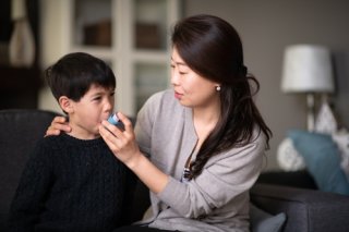 A mother helps her young son use an inhaler