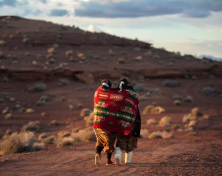 Two indigenous women walk along a dusty path.