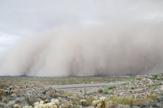 A large dust storm approaches across a sagebrush landscape.