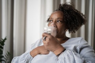An African-American woman uses a nebulizer.