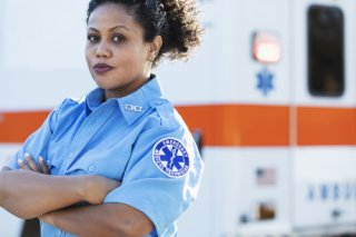 Young African-American paramedic stands in front of an ambulance with an orange stripe.