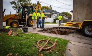 Men standing around a hole in the street and replacing a water line