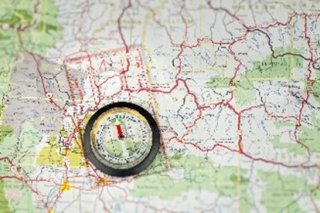 A clear compass sitting on a map with red end of arrow pointing upward