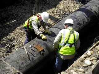 Technicians in personal protective equipment prepare pipe before cutting and removing the section from the Enbridge pipeline oil spill site near Marshall, Michigan.