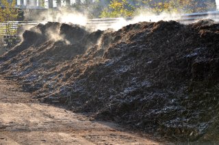 This is a picture of large mounds of almost finished compost that appear to be smoking at an industrial facility