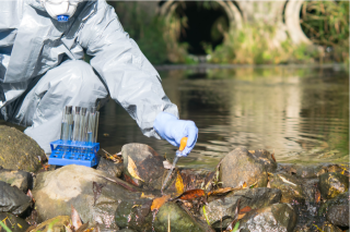 Scientist in decontamination suit taking water samples in creek