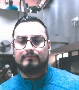 headshot of middle age latino male wearing glasses. facial hair is a short beard and musctache