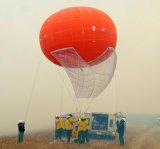 Image of a group of people standing next to a truck launching a large orange monitoring balloon in dense smokey air