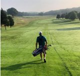 A man carrying a golf bag, walking along a golf course