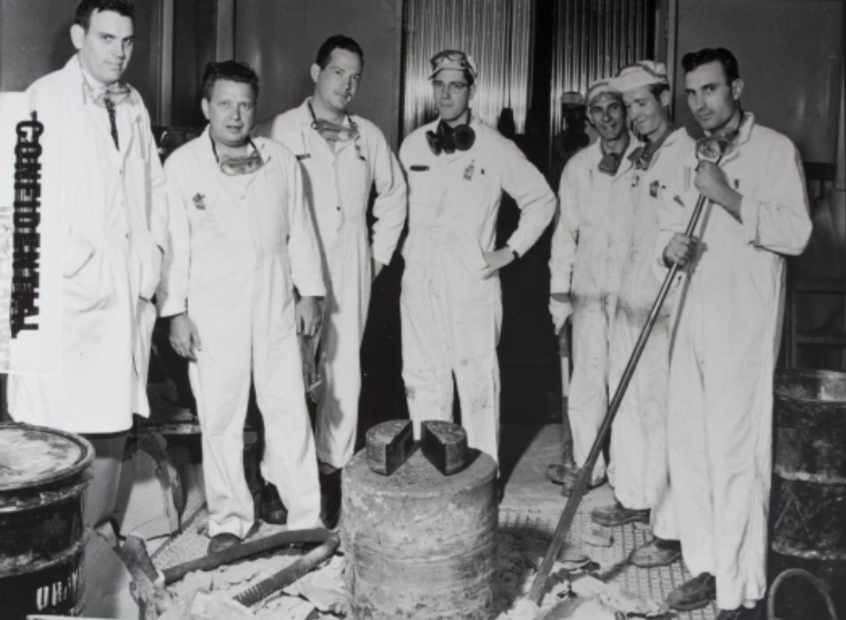 Historic photo of a group of people in white coveralls in a processing facility