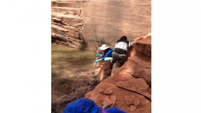 Workers at base of a cliff extracting water from a pool