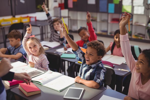 kids raise their hands to answer a question in class