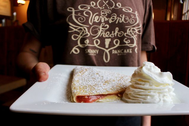 This is a picture of a Skinny Pancake worker holding a plate with a pancake and whip cream.