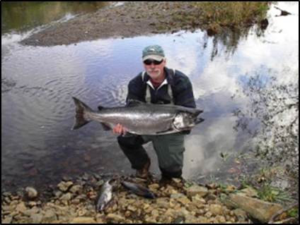 An older man wearing a green hat and sunglasses holds a two-foot-long silver fish that he caught