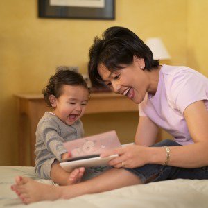 Woman smiling and she reads book to baby.